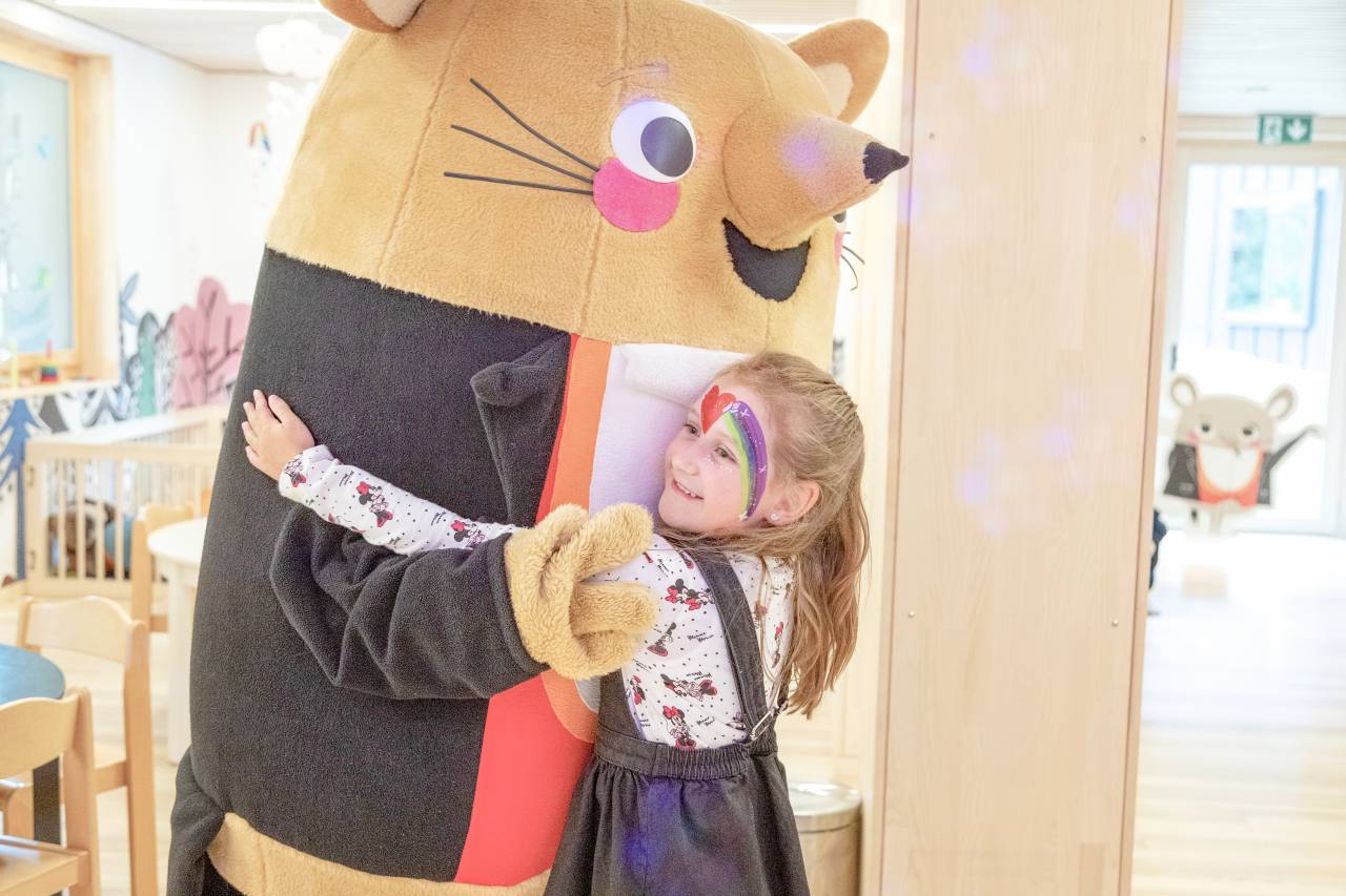 Mädchen mit Kinderschminke umarmt Maskottchen Herr Gorfion