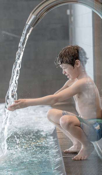 Kind am Pool-Wasserfall im Wellnessbereich des Familienhotel Gorfion Liechtenstein