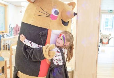 Mädchen mit Kinderschminke umarmt Maskottchen Herr Gorfion